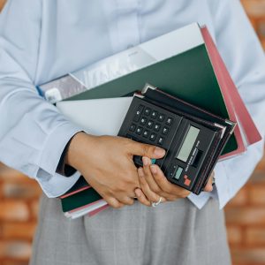 Mains d'une femme debout qui tient des affaires dont des classeurs et une calculatrice